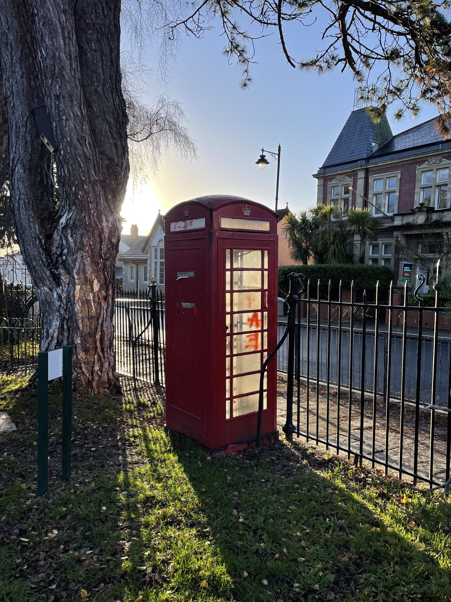 A red telephone box by the railings at the Albert Road entrance to Belle Vue Park