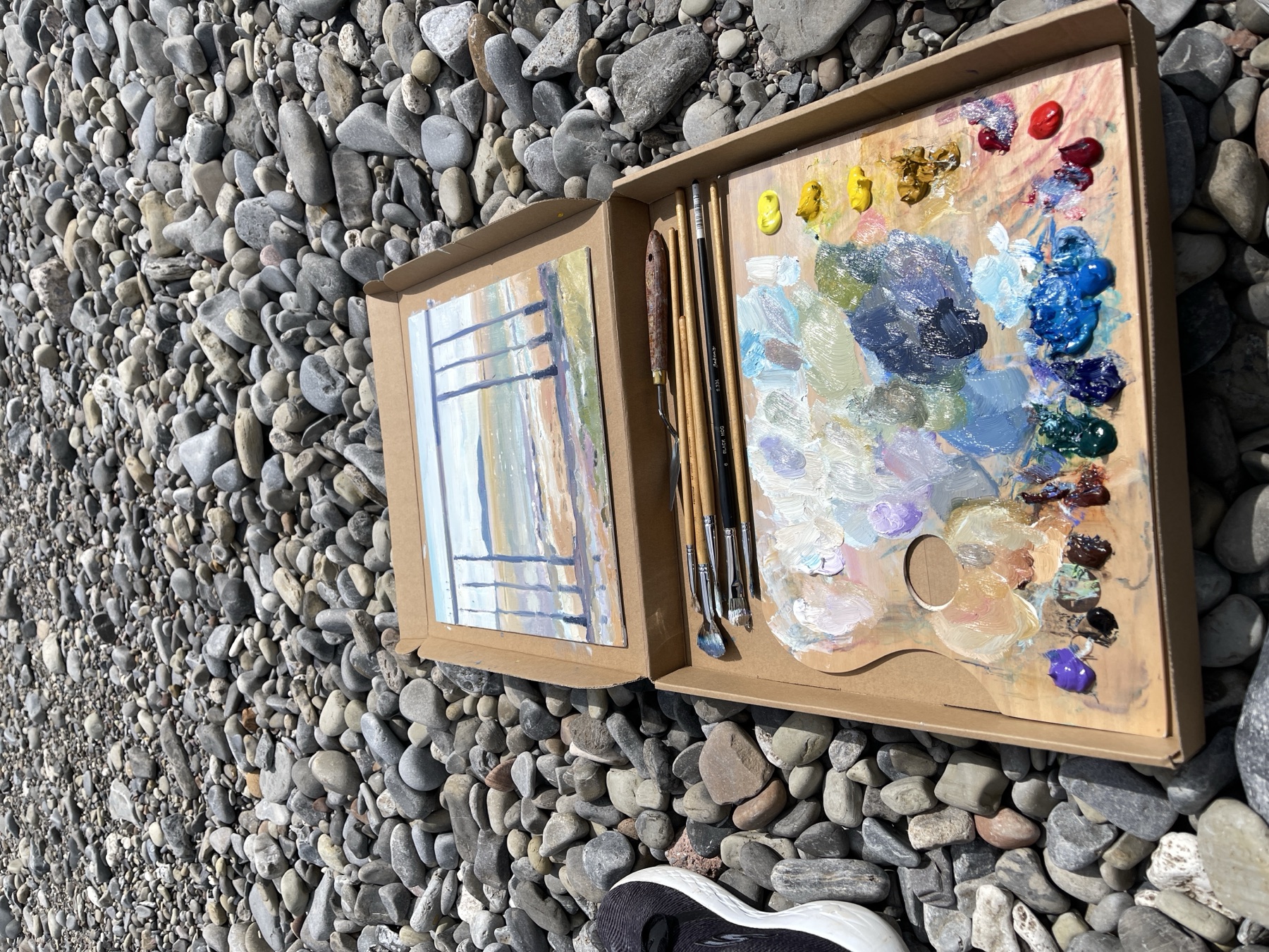 Plein air oil painting box on the beach with brushes and a painted seascape