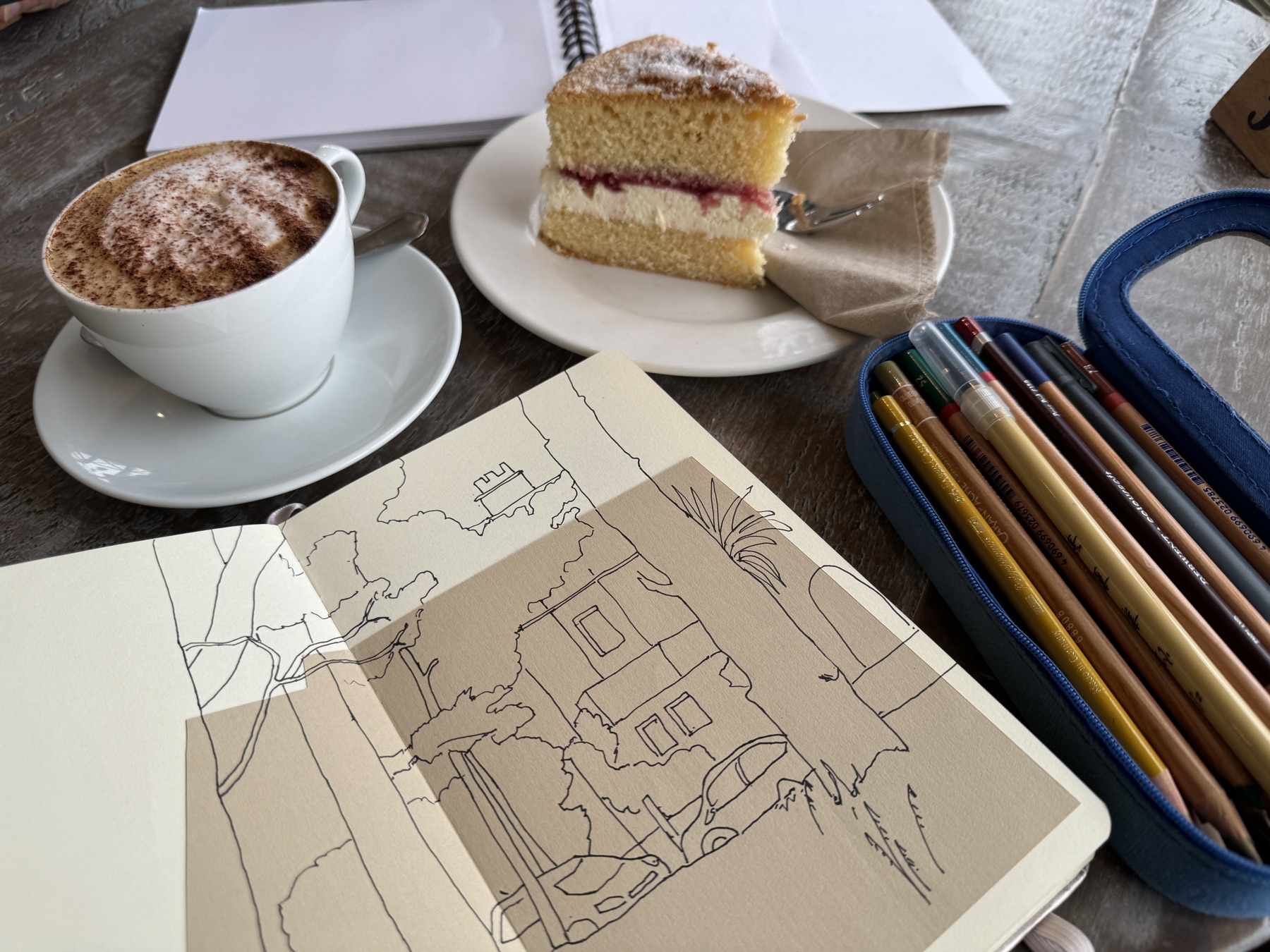 Sketchbook, cake, coffee, and coloured pencils on a table